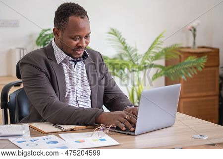 African American Businessman Analyzing Laptop Graph Paperwork In Office Holding Documents