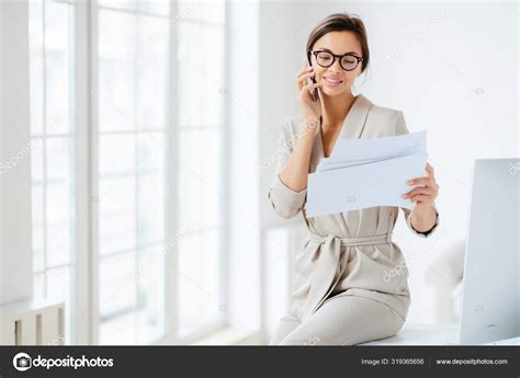 Attractive Businesswoman Reads Papers Or Business Documents Has Telephone Talk With Business