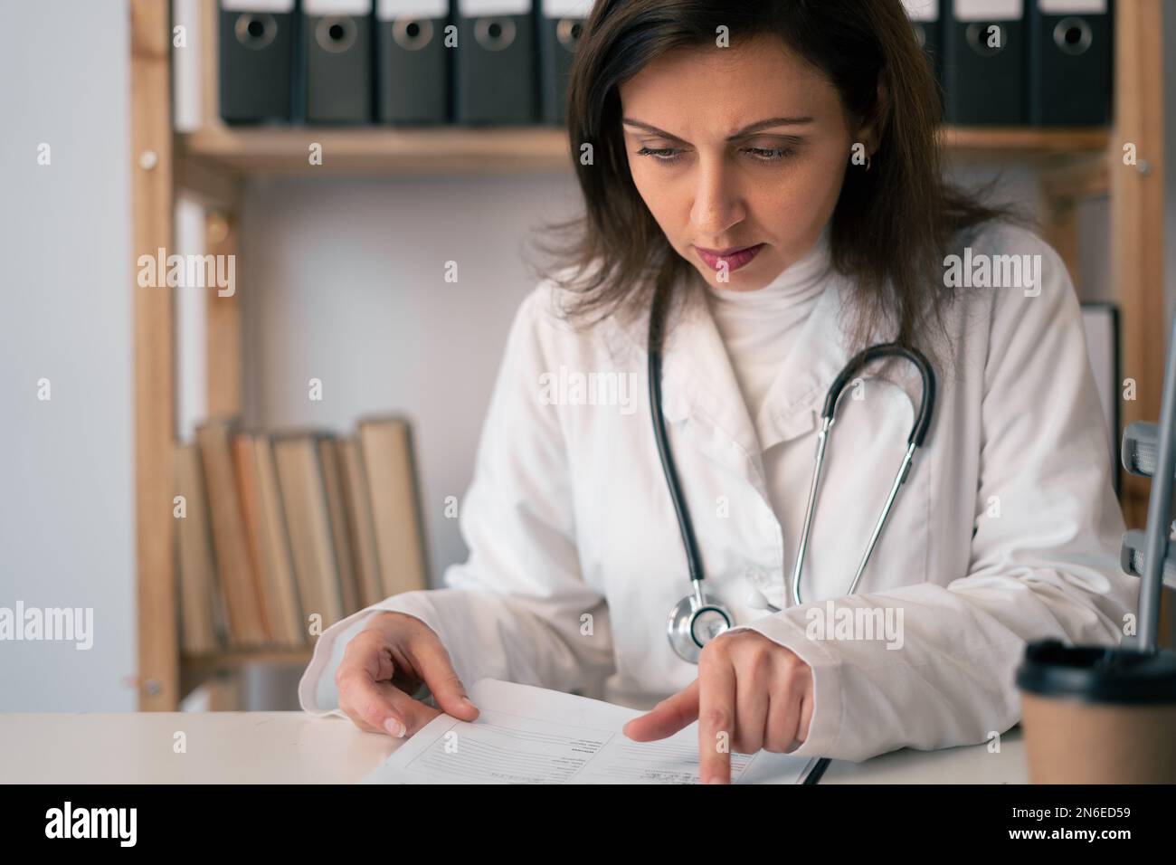 Concentrated Female Doctor Reading Document At Table In Clinic Doctor