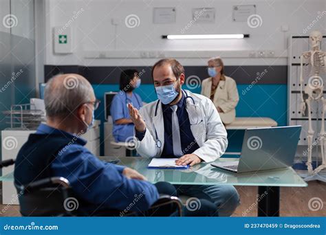 Doctor Consulting Elder Man With Physical Disability In Office Stock