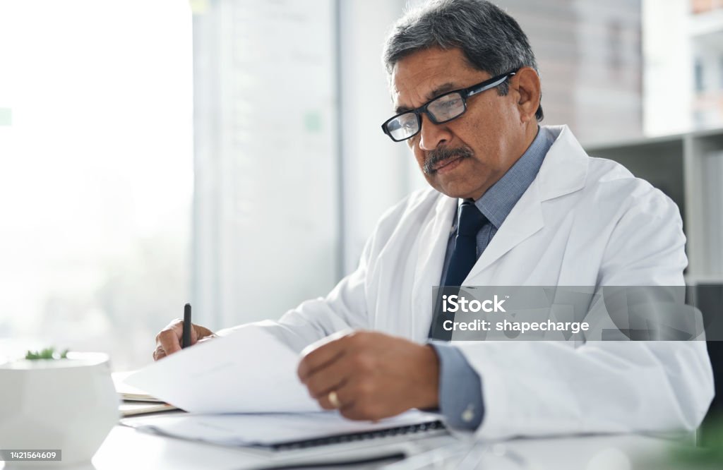 Doctor Doing Medical Paperwork In His Office At The Clinic While