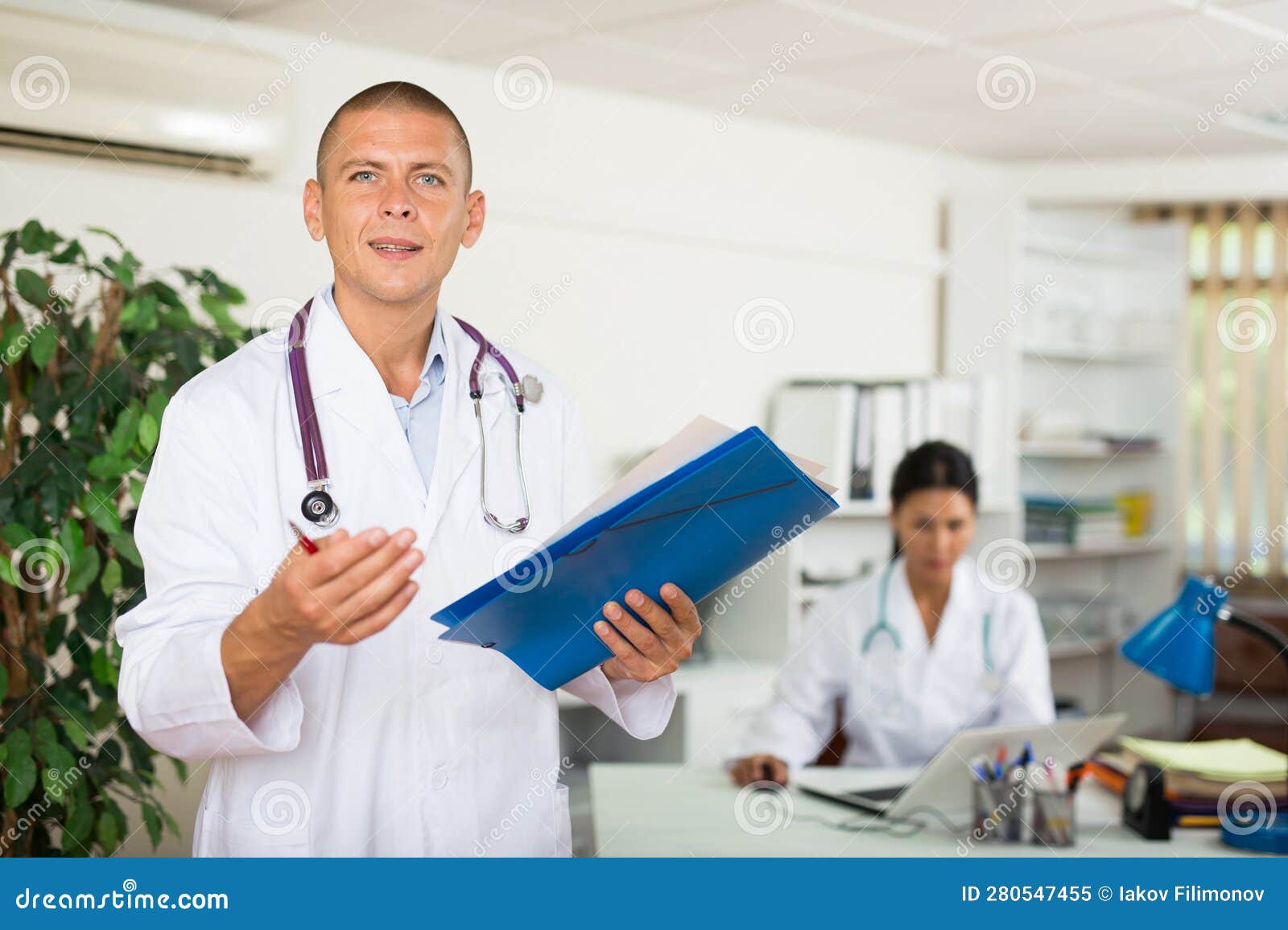 Doctor Filling Out Medical Form At Clipboard In Clinic Office Stock