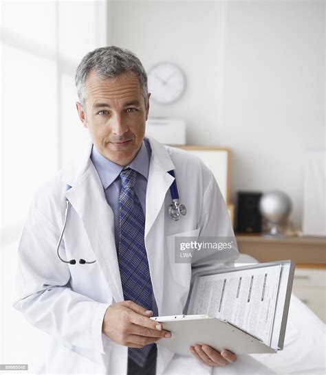 Doctor Holding Paperwork In Examination Room High Res Stock Photo