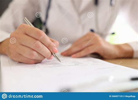 Female Doctor Fills Out Medical Forms While Sitting At Her Desk In