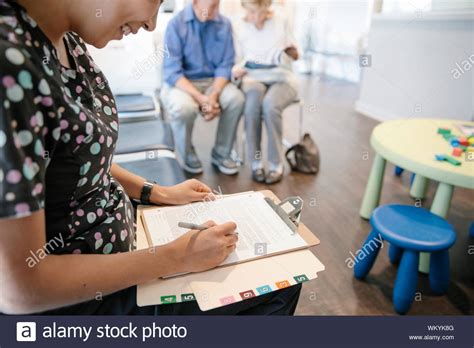 Female Nurse Filling Out Paperwork In Clinic Waiting Room Stock Photo