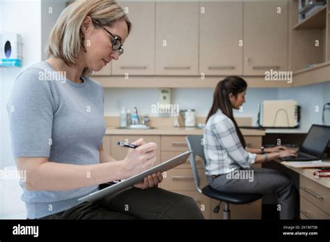 Female Patient Filling Out Paperwork In Clinic Exam Room Stock Photo