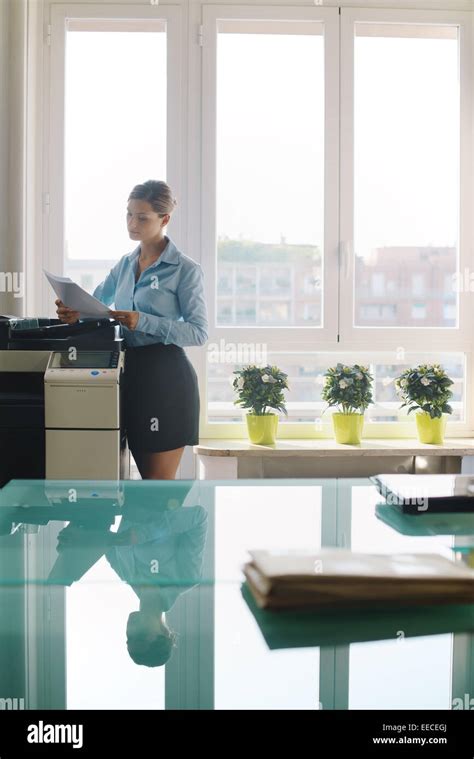 Female Secretary Working In Office Copying Document And Paperwork With Copy Machine In Modern