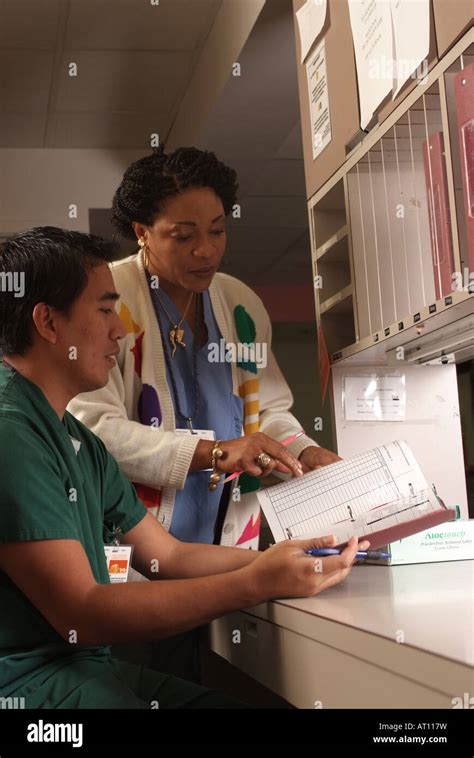 Heath Care Two Nurses Look Over Paperwork At The Nurses Station Stock