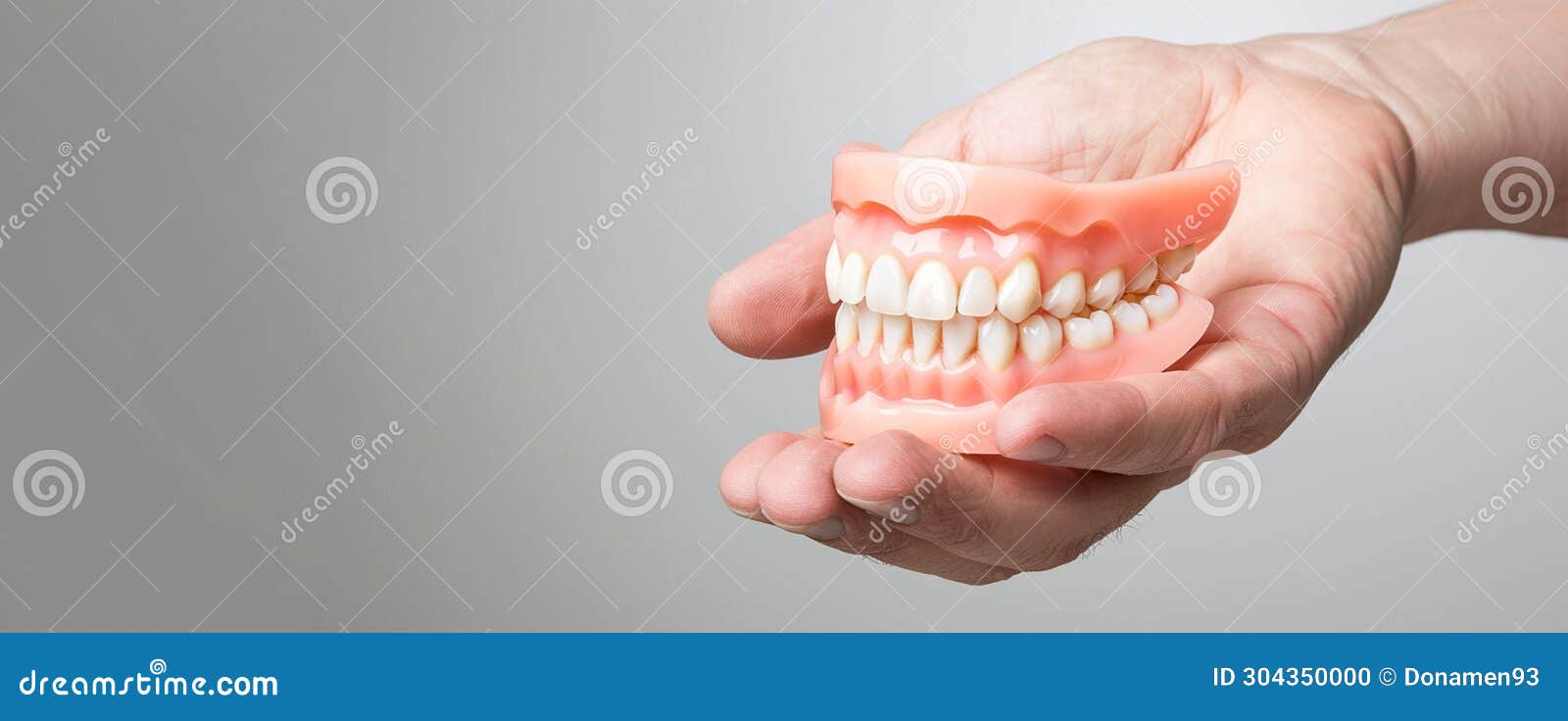 Human Hand Holding Complete Upper And Lower Denture Set On Neutral