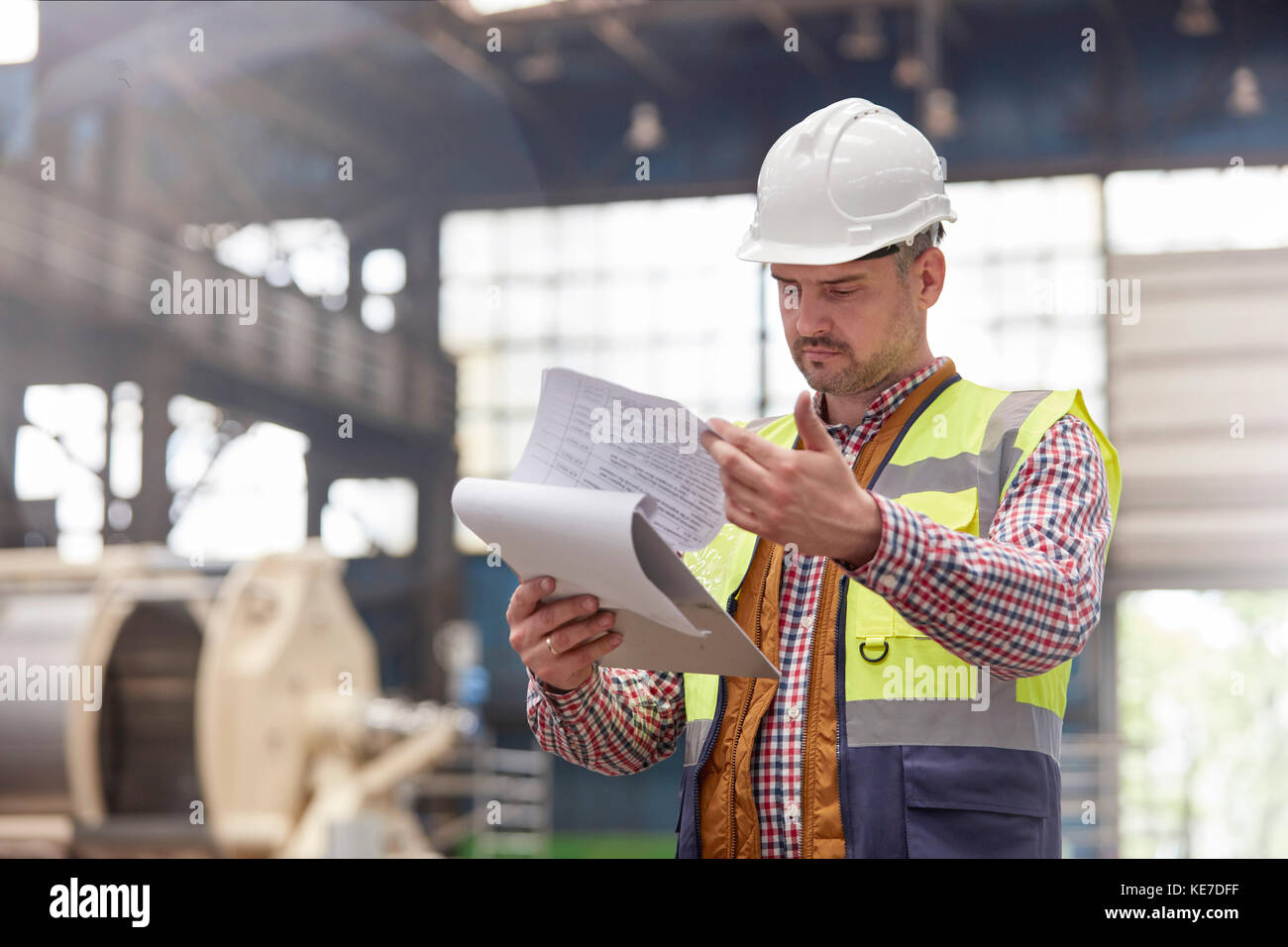 Male Foreman Reviewing Paperwork On Clipboard In Factory Stock Photo