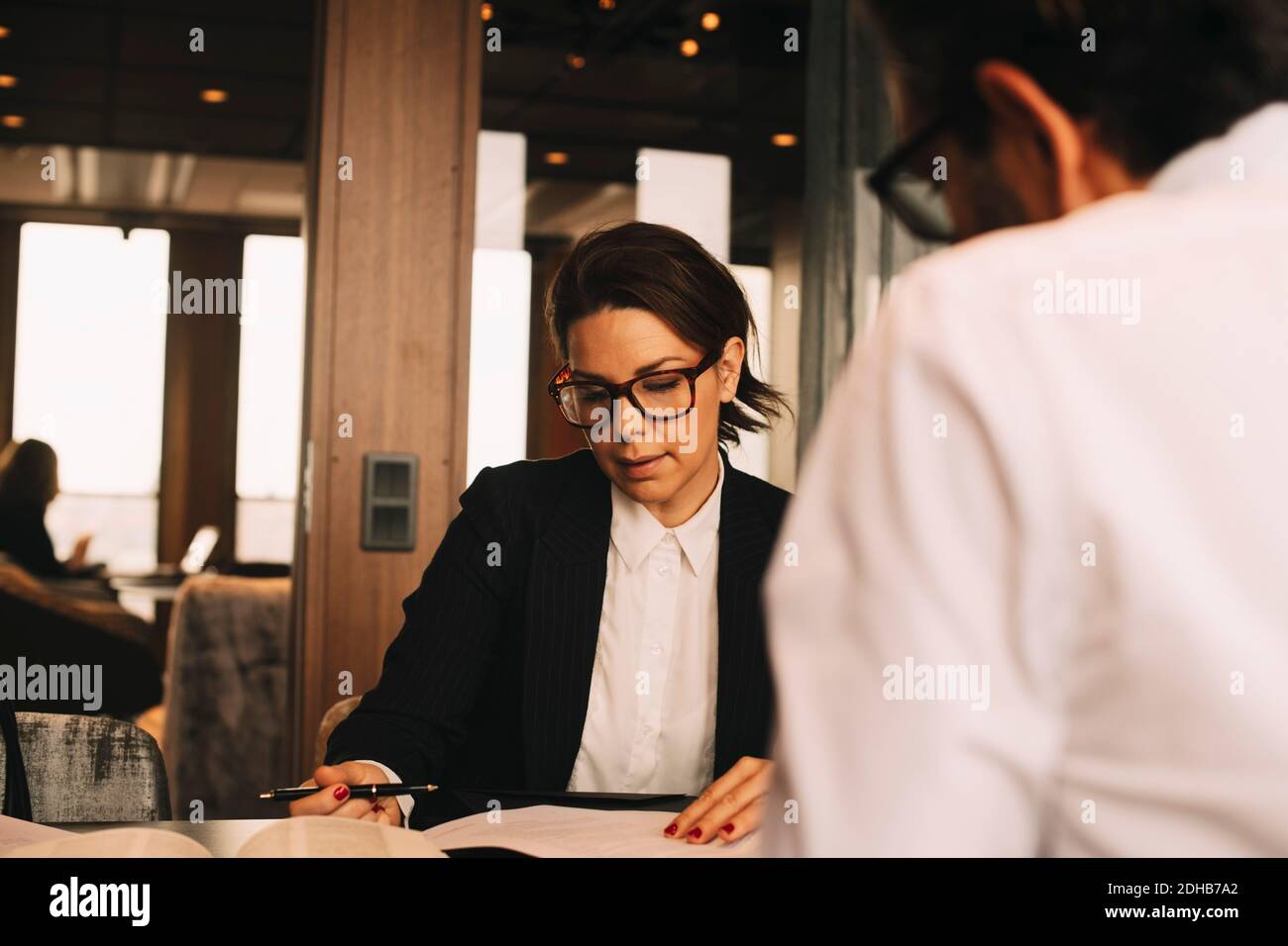 Mid Adult Female Lawyer Discussing Paperwork With Client At Table In