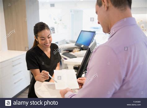 Nurse Reviewing Paperwork With Patient At Clinic Reception Stock Photo