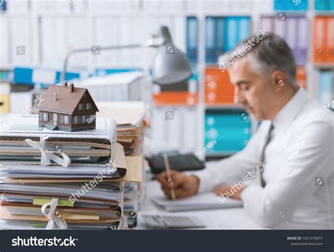 Real Estate Agent Working In The Office And Piles Of Paperwork Model