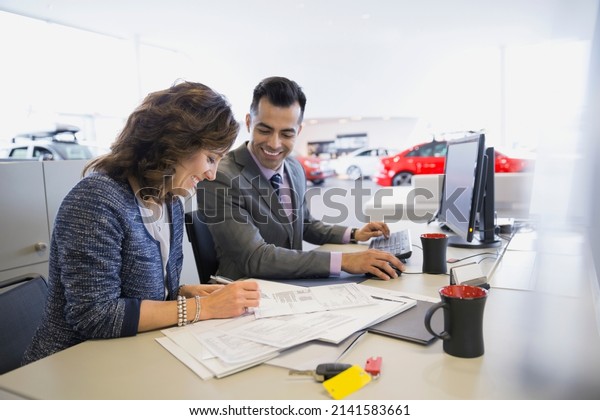 Salesman And Woman Finalizing Paperwork In Car Dealership Stock Photo