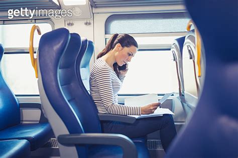 Young Woman Traveling By Train Using Mobile Phone And Browsing Paper